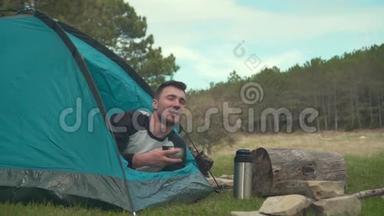 一个年轻人躺在森林里的蓝色帐篷里，喝着热水瓶里的<strong>茶</strong>，享受着这一刻。